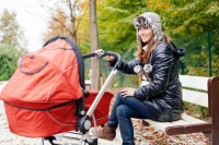 Young woman sitting on park bench with baby in stroller