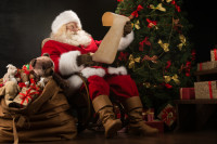 Portrait of happy Santa Claus reading Christmas letter or wish l