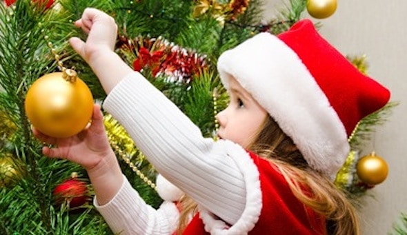 Little girl in santa hat decorating the christmas tree