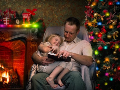 Christmas story by the fireplace. Dad reads a book a little daughter. Christmas tree, festive interior of the house. Christmas Eve